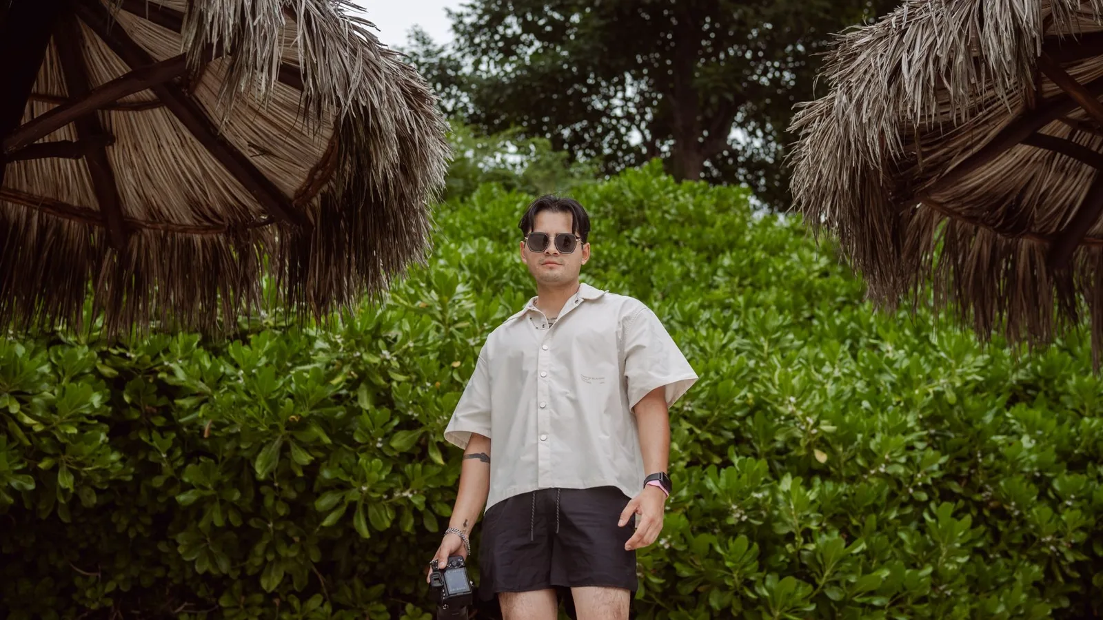A photographer in beach attire holding a camera, surrounded by lush tropical greenery in Punta Mita.