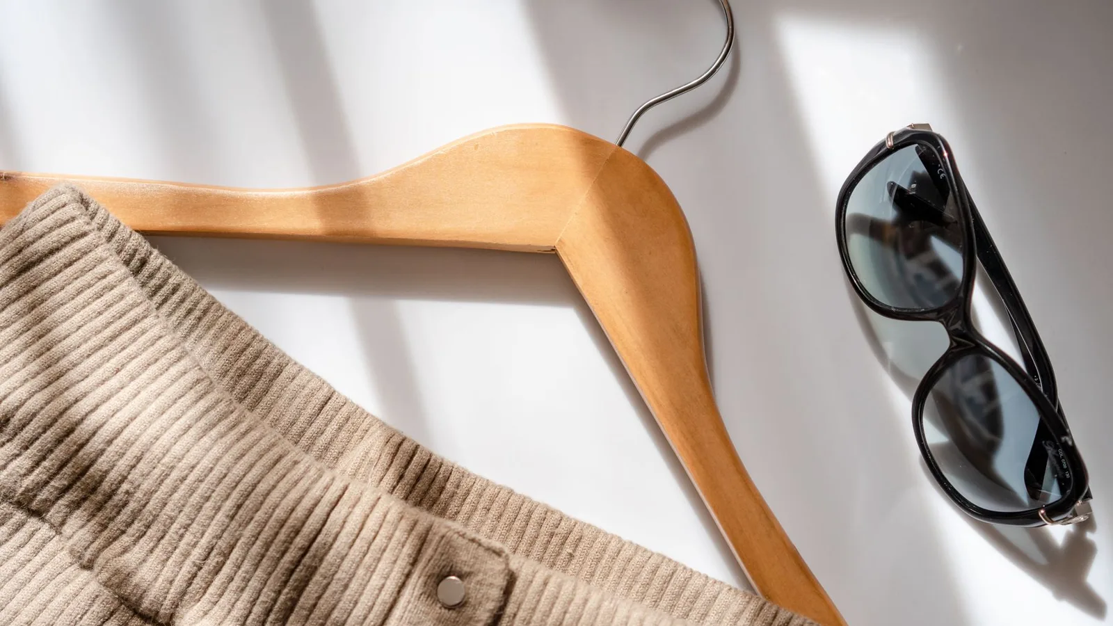 Flat lay of a corduroy skirt, sunglasses, and a wooden hanger on a white surface.