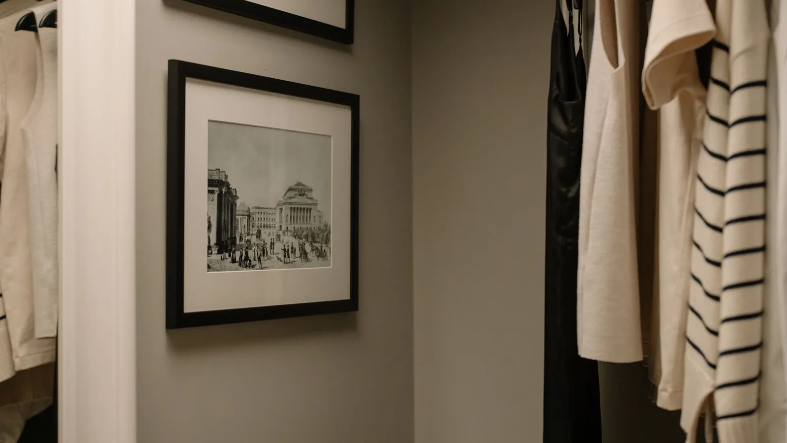 A well-organized closet with hanging clothes and vintage framed photographs for a modern minimalist look.