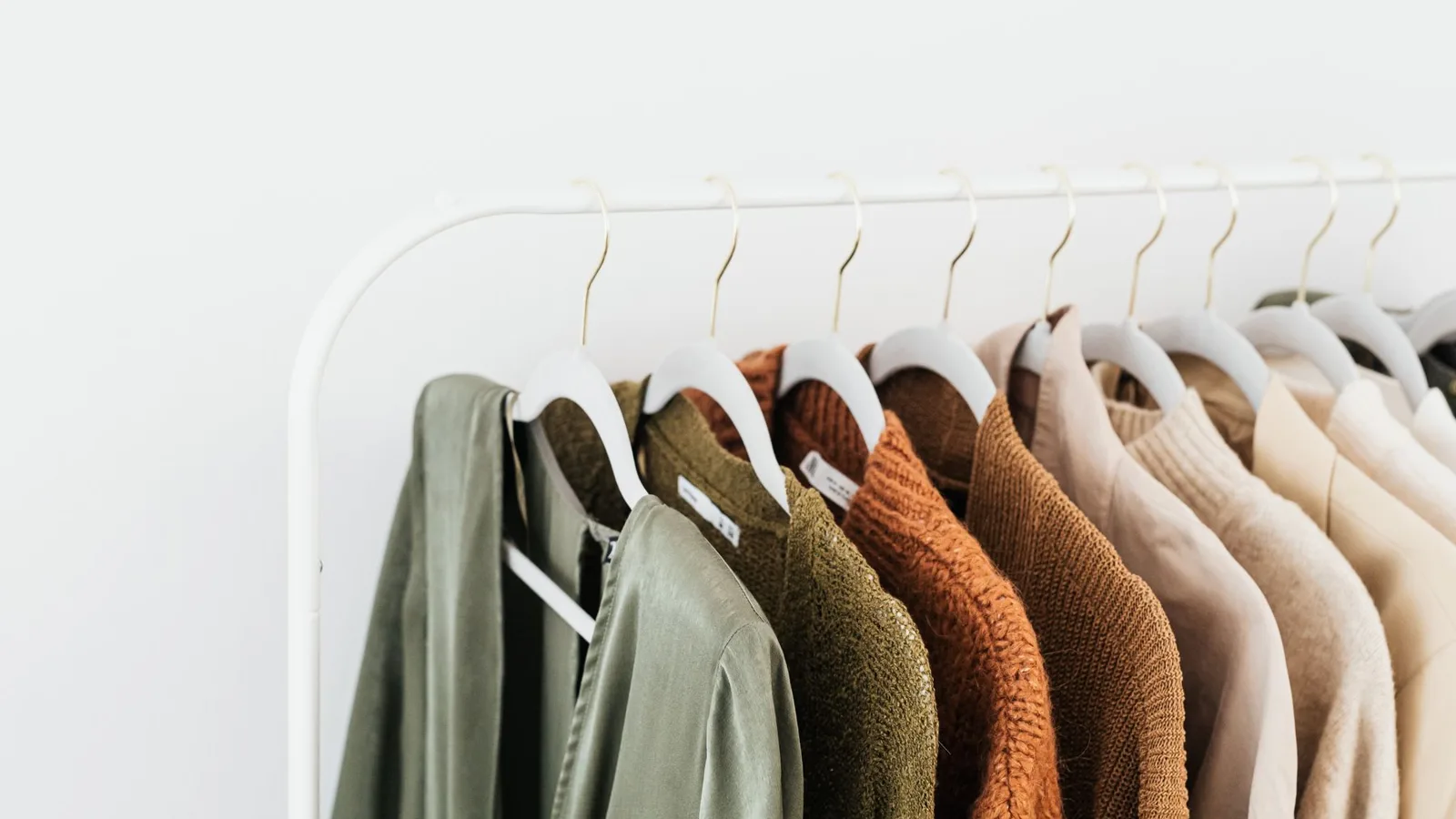 A minimalist display of colorful sweaters and shirts on white hangers.