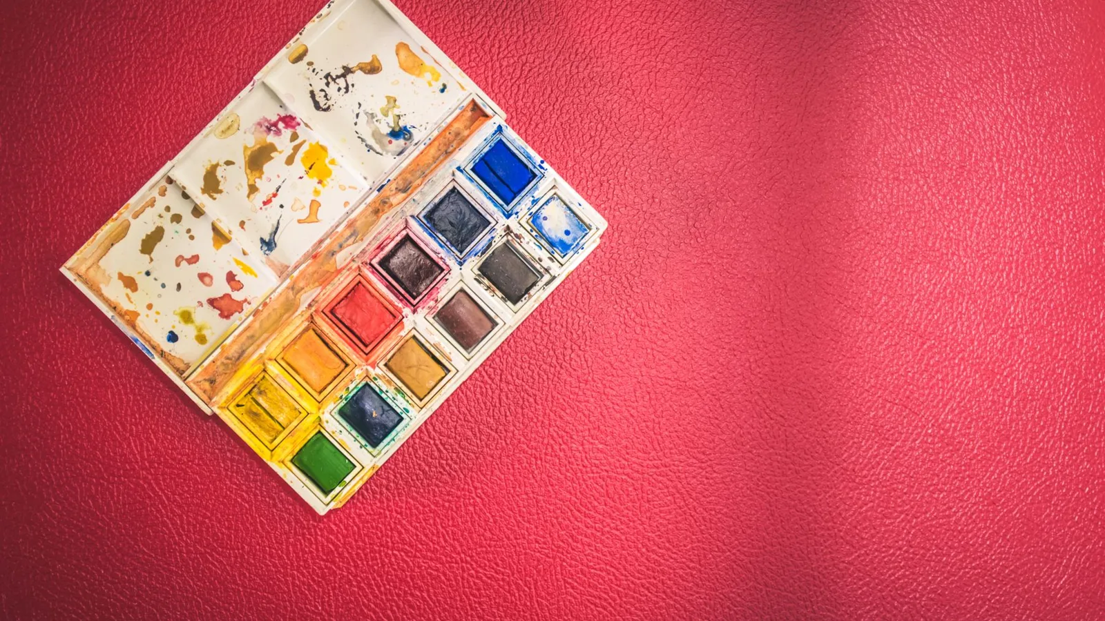 A top view of a vibrant watercolor paint set on a textured red background, perfect for creativity.