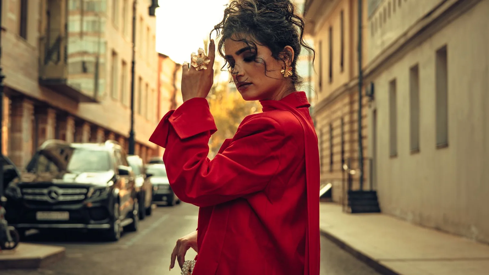 Fashionable woman in a red dress posing confidently on an urban street.