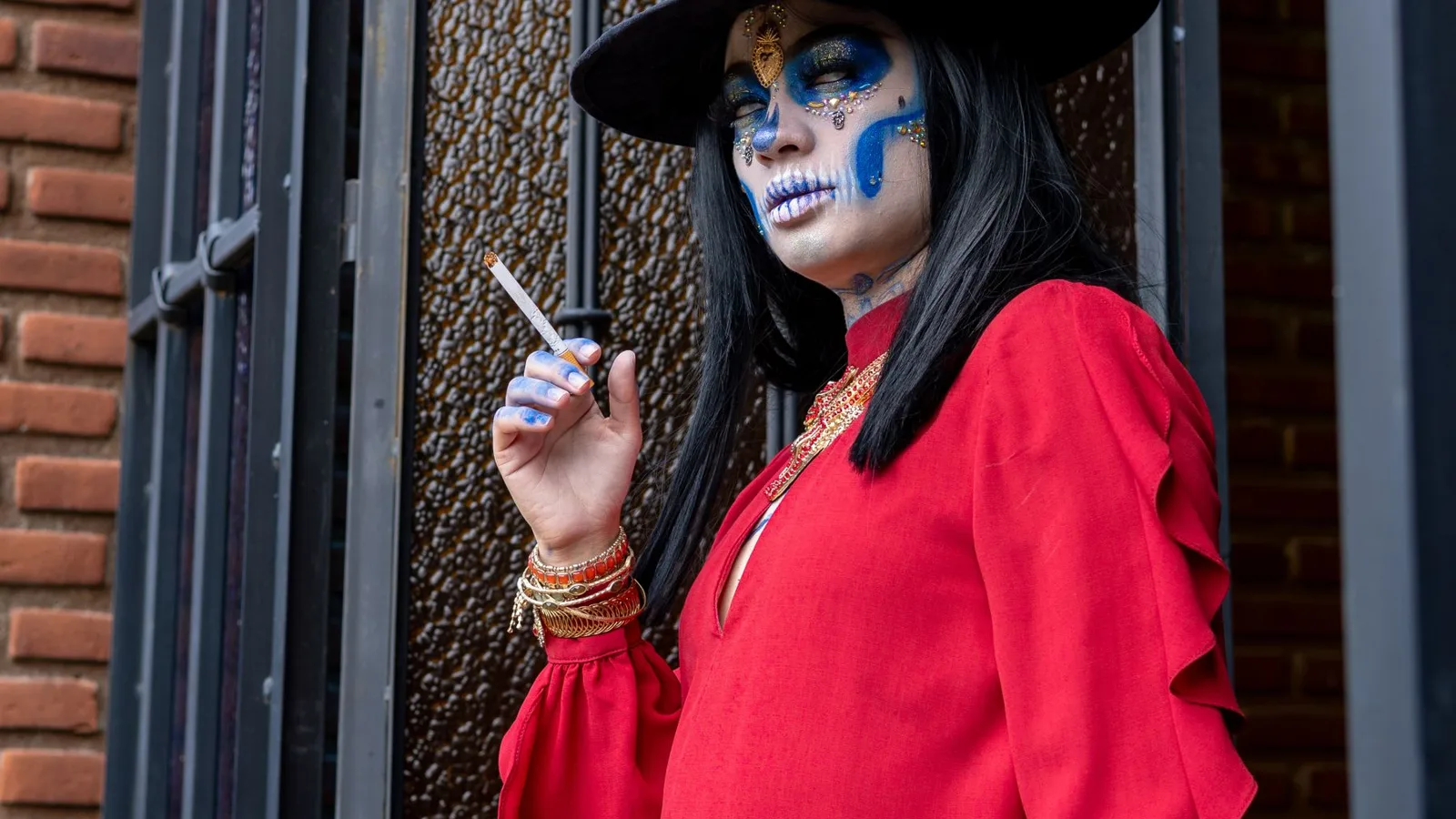 Striking portrait of a woman in artistic Day of the Dead makeup, wearing a vibrant red outfit in an urban setting.