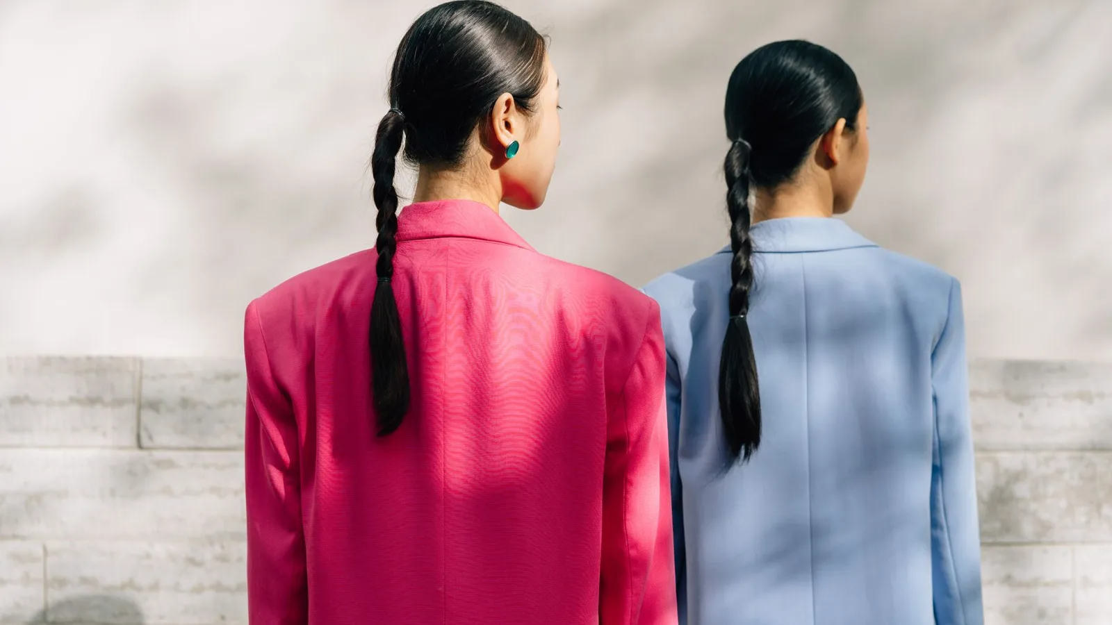 Two women in bright blazers facing a textured wall.