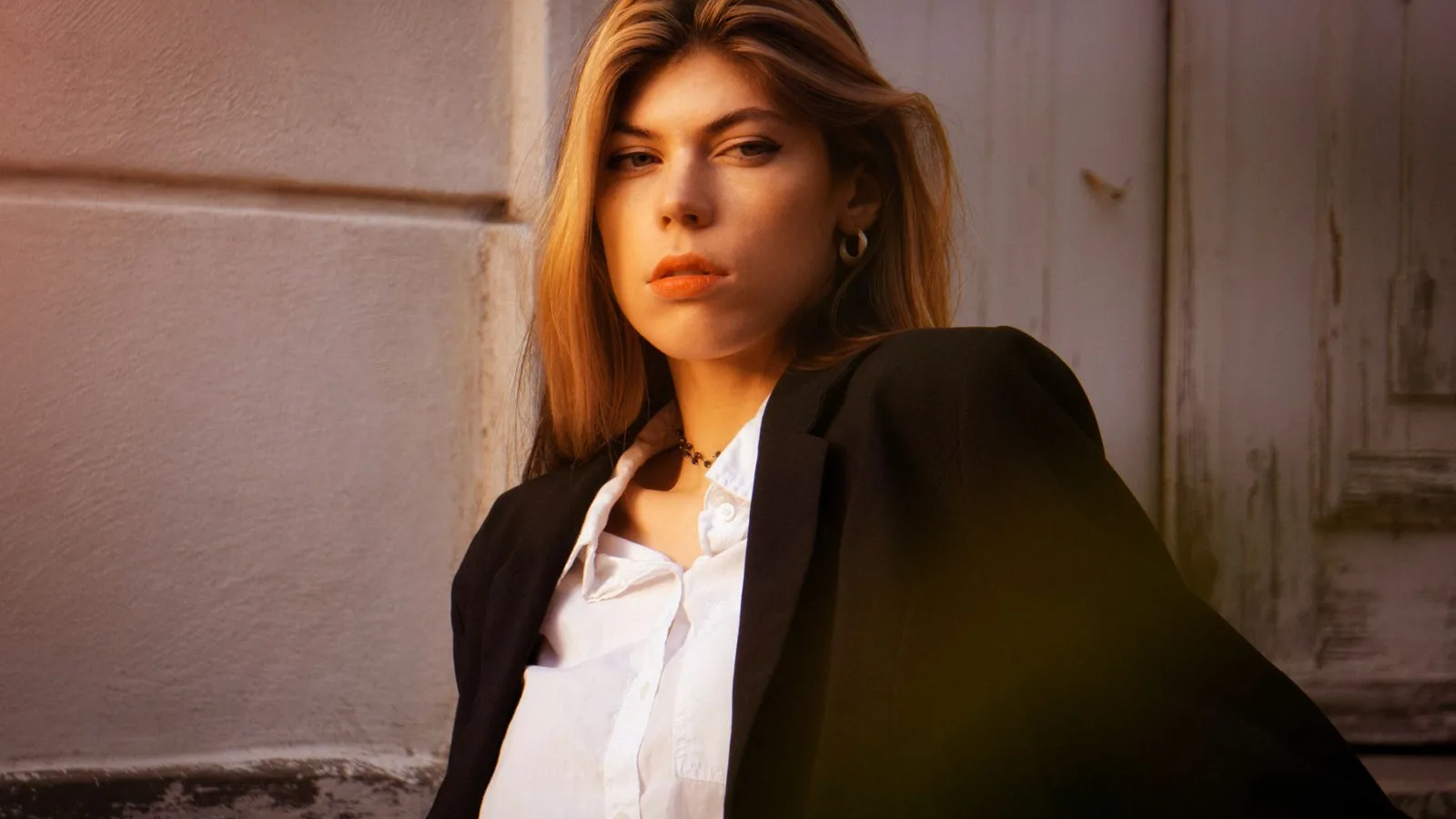 Stylish young woman in blazer posing confidently in soft outdoor light.