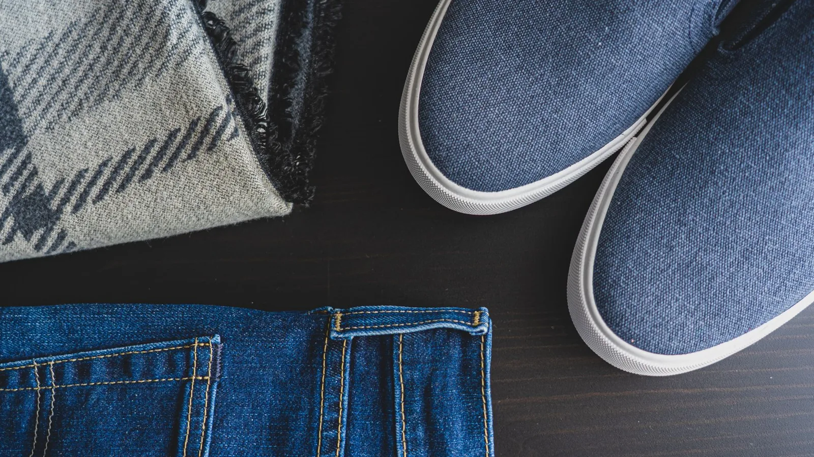 Flat lay of denim jeans, blue sneakers, and a plaid scarf for a casual look.