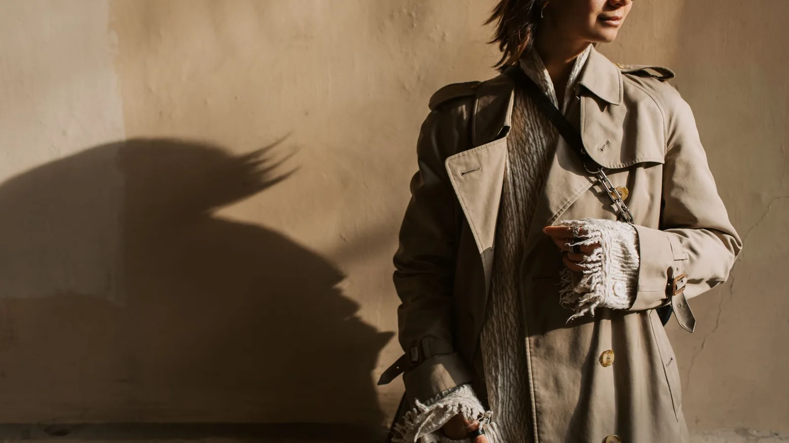 Fashionable woman in a trench coat posing with dramatic shadows in the fall sun.