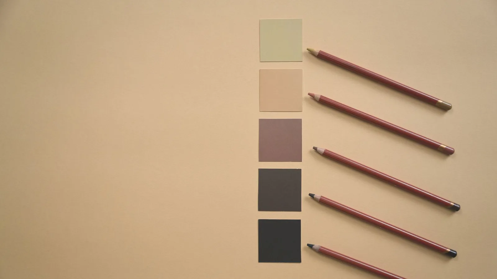 Flat lay of colored pencils and earthy tone swatches on a beige background, perfect for art and design contexts.