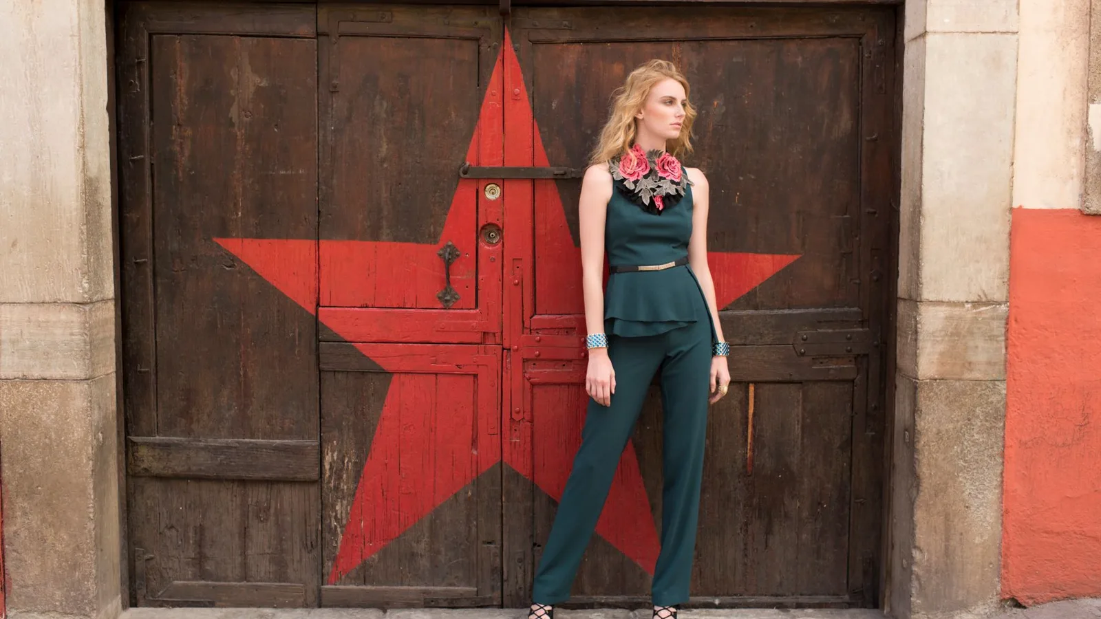 Stylish woman in a green outfit poses confidently by a rustic door with a red star.