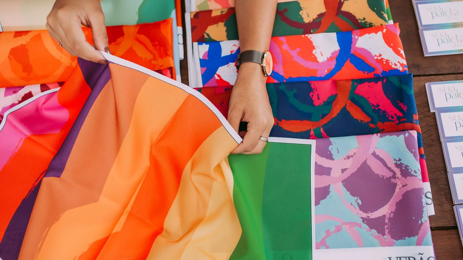Close-up of hands handling vibrant fabric samples, showcasing diverse patterns and colors.