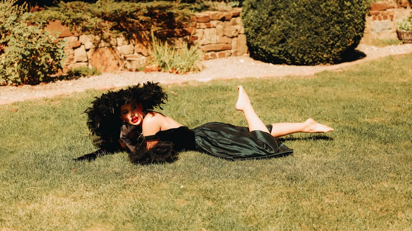 A woman in an extravagant black dress lounging on a sunny lawn, exuding elegance.
